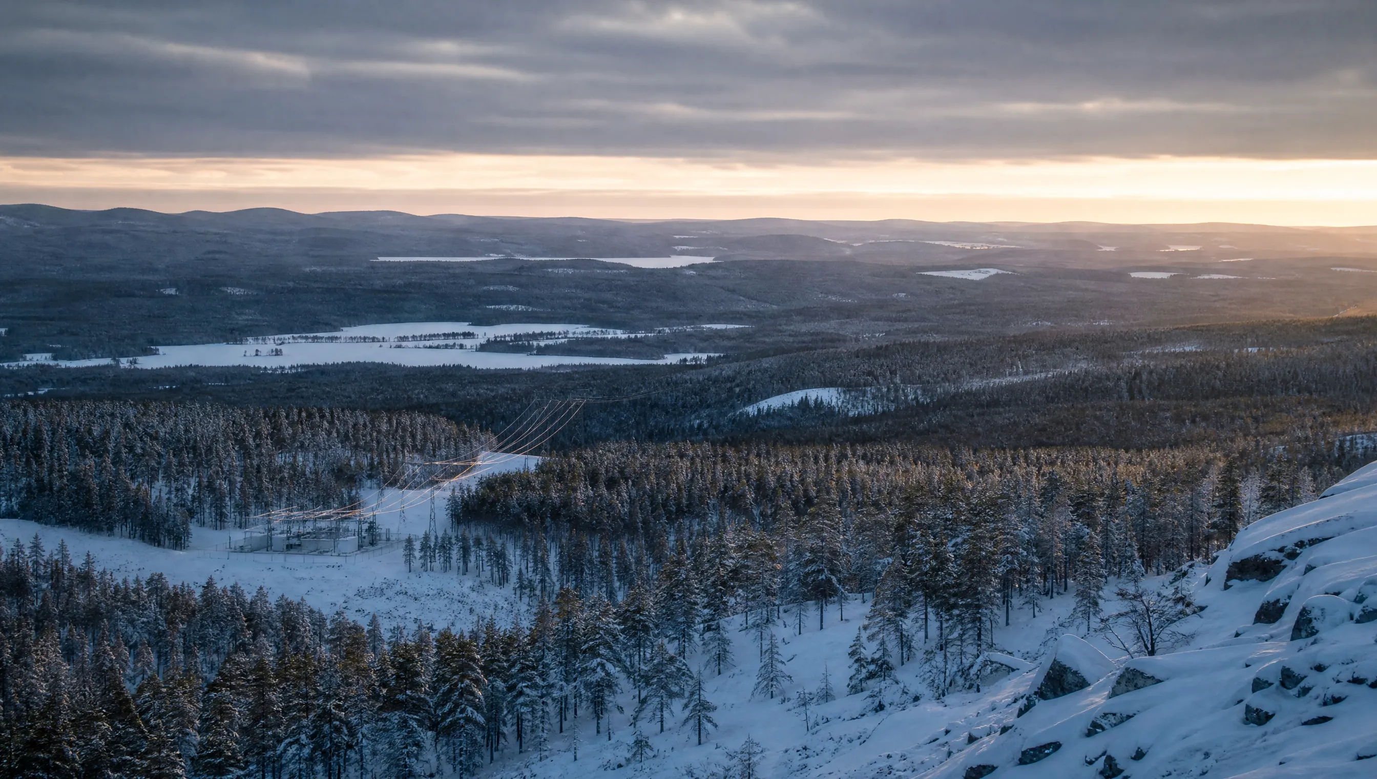 A Nordic winter landscape at dawn, transmission lines descending into a forested valley